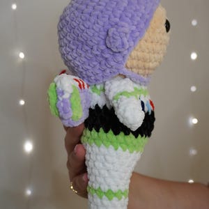Puede incluir: Mu&ntilde;eco de Buzz Lightyear tejido a ganchillo. El mu&ntilde;eco presenta un casco lavanda, una cara bronceada y un traje espacial blanco, verde y negro. El mu&ntilde;eco est&aacute; hecho de hilo suave y texturizado y es un art&iacute;culo hecho a mano.