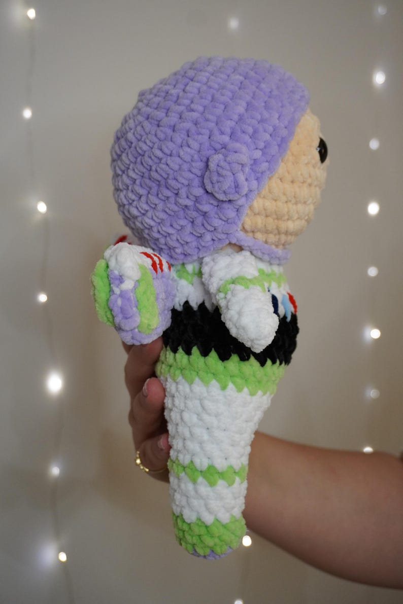 Puede incluir: Mu&ntilde;eco de Buzz Lightyear tejido a ganchillo. El mu&ntilde;eco presenta un casco lavanda, una cara bronceada y un traje espacial blanco, verde y negro. El mu&ntilde;eco est&aacute; hecho de hilo suave y texturizado y es un art&iacute;culo hecho a mano.