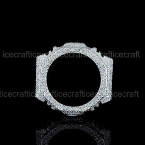 May include: A silver ring with a square design and a circular aperture. The ring is covered in many small, sparkling stones. The background is black, and the ring is reflected in the surface below.