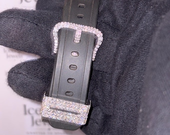Peut inclure: Gros plan sur un bracelet de montre noir avec une boucle et une extrémité de bracelet incrustées de diamants étincelants. La boucle est de conception classique, et le bracelet comporte plusieurs trous de réglage. Le bracelet est tenu par une main gantée.