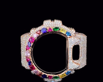 May include: A rose gold watch bezel encrusted with numerous small, clear crystals and a variety of colorful gemstones. The gemstones include pink, blue, green, and yellow. The watch bezel is set against a black background.