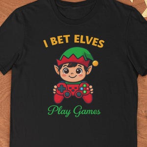 May include: Black t-shirt with a cartoon elf holding a red video game controller. The text "I BET ELVES" is above the elf, and "Play Games" is below. The elf wears a green hat.
