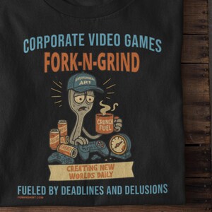 May include: Black t-shirt with a humorous graphic. The design features a fork character wearing a cap and holding a coffee mug and a game controller. Text includes "CORPORATE VIDEO GAMES FORK-N-GRIND" and "FUELED BY DEADLINES AND DELUSIONS."