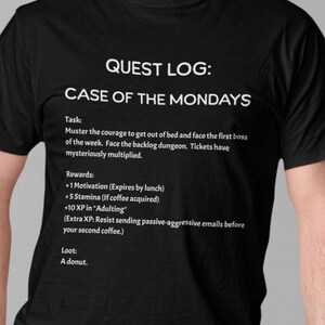 Pode incluir: Camiseta preta com texto branco. O texto diz "QUEST LOG: CASE OF THE MONDAYS." O texto abaixo detalha uma "Tarefa" e "Recompensas", incluindo "+1 Motivação" e "+5 Resistência." O "Saque" é listado como "Uma rosquinha."