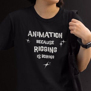 以下が含まれることがあります： 黒いクルーネックTシャツ。白で「ANIMATION BECAUSE RIGGING IS BORING」のテキストと星のグラフィック。カジュアルウェアです。