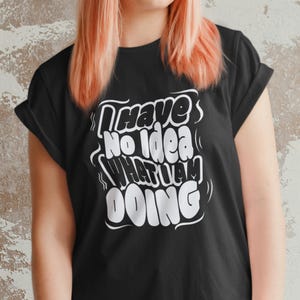 May include: Black t-shirt with the white text "I Have No Idea What I Am Doing" in a bold, stylized font. The shirt has short sleeves and a crew neck. The model is wearing the shirt.