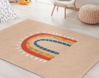 May include: A rectangular beige rug with a colorful rainbow design. The rainbow features red, orange, yellow, and blue arches, with white dotted accents. The rug is placed in a child's playroom, with a teepee and toys visible.