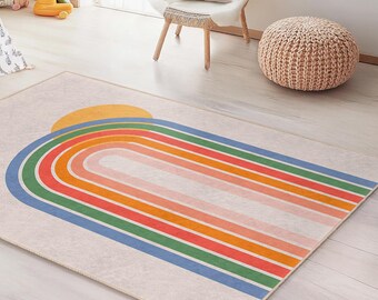 May include: A rectangular area rug with a rainbow design. The rug features a beige background with a large rainbow arch in shades of blue, green, orange, and red, topped with a yellow sun. The rug is placed in a child's room.