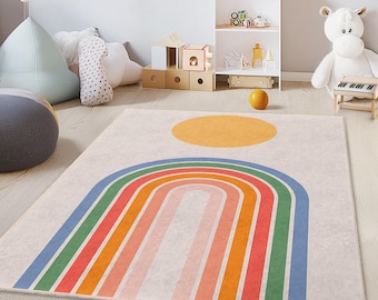 May include: A rectangular area rug with a rainbow design and a yellow sun. The rug features a cream-colored background with a large rainbow in shades of red, orange, green, and blue. The rug is likely made of a soft material and is suitable for a child's room.