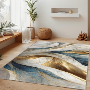 Può includere: Un tappeto rettangolare con un design simile al marmo. Il tappeto presenta una miscela di tonalità bianche, dorate e blu, creando un motivo astratto e fluido. Il tappeto è posizionato su un pavimento in legno in un soggiorno.