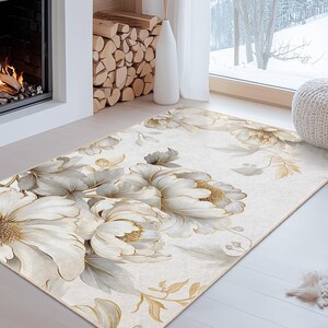 May include: A rectangular area rug featuring a floral design with large white and gold flowers. The rug has a cream-colored background and is placed on a light-colored wooden floor. The room has a fireplace and a large window.