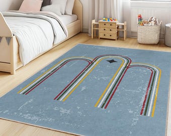 May include: A light blue rectangular rug with a retro design in a child's bedroom. The rug features three arched lines in red, white, yellow, and green, with a black star in the center. The rug is placed on a light wood floor.