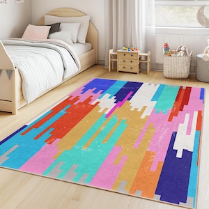 May include: A rectangular area rug with a colorful geometric design. The rug features a pattern of vertical stripes in shades of blue, red, orange, yellow, pink, and white. The rug is placed on a light-colored wooden floor in a child's bedroom.