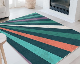 Op de afbeelding: Een geometrisch vloerkleed met een sunburst-ontwerp. Het kleed heeft strepen in teal, koraal, groen, paars en wit die uitstralen vanuit een hoek. Het kleed ligt op een lichtgekleurde vloer in een woonkamer.