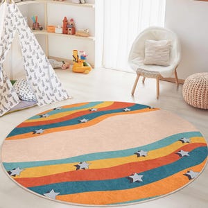 May include: A round rug with a colorful rainbow design in shades of orange, teal, yellow, and blue. The rug features a light beige center and scattered gray stars. This rug is perfect for a child's room or playroom.