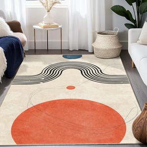 Op de afbeelding: Een rechthoekig vloerkleed met een abstract ontwerp. Het vloerkleed heeft een grote oranje cirkel, een zwart-wit gebogen lijnenontwerp en een blauwe halve cirkel. De achtergrond is crèmekleurig.
