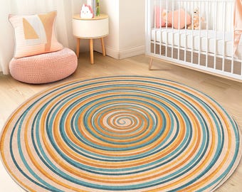Op de afbeelding: Een ronde vloerkleed met een spiraalvormig ontwerp. Het vloerkleed heeft concentrische cirkels in tinten beige, blauwgroen en oranje. Het ligt op een houten vloer in een kamer met een wieg en een kleine bijzettafel.