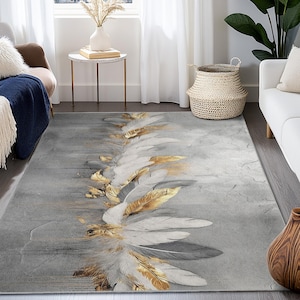 Puede incluir: Una alfombra rectangular con un fondo gris y un diseño de plumas estilizadas en blanco, dorado y gris. Las plumas están dispuestas en un patrón en forma de abanico sobre la superficie de la alfombra. La alfombra está en un salón.