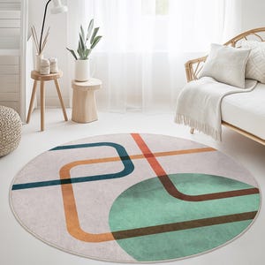 Op de afbeelding: Rond vloerkleed met een geometrisch ontwerp. Het vloerkleed heeft een lichtbeige achtergrond met turquoise, oranje en bruine lijnen en een turquoise groene cirkel. Zachte, decoratieve vloerbedekking.