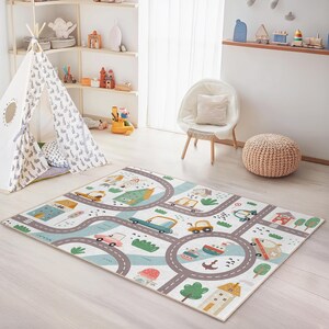 May include: A rectangular children's play rug featuring a road map design with cars, houses, trees, and water elements. The rug has a white background with gray roads and colorful illustrations. The rug is designed for a child's playroom.
