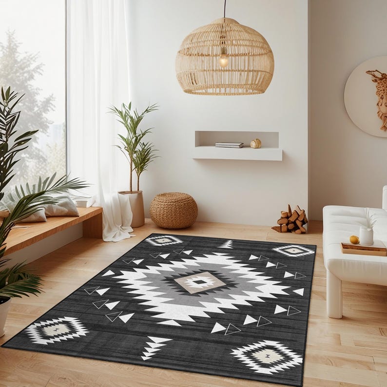 K&ouml;nnte beinhalten: Rechteckiger Teppich mit geometrischem Muster in Schwarz, Wei&szlig;, Grau und Beige. Der Teppich hat ein zentrales Rautenmuster und sich wiederholende Dreiecksformen. Der Teppich liegt auf einem Holzboden in einem Wohnzimmer.
