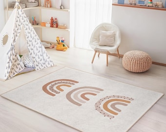 May include: A rectangular area rug with a cream background and three stylized rainbow designs in shades of brown. The rug is in a child's playroom, with a teepee, chair, and pouf visible.