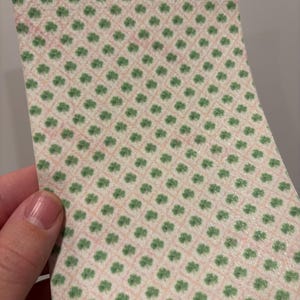 Może przedstawiać: Kawałek wzorzystego papieru z powtarzającym się wzorem zielonych koniczynek na jasnor&oacute;żowym i beżowym tle. Koniczynki ułożone są w siatkę.