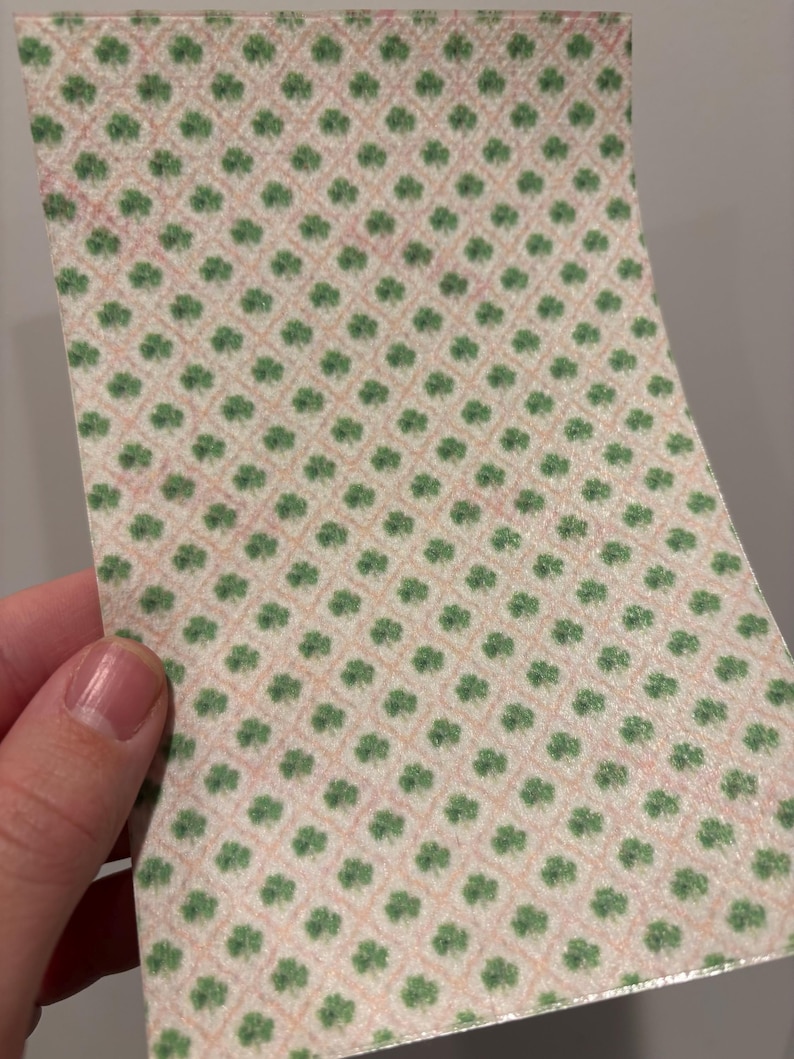 Może przedstawiać: Kawałek wzorzystego papieru z powtarzającym się wzorem zielonych koniczynek na jasnor&oacute;żowym i beżowym tle. Koniczynki ułożone są w siatkę.