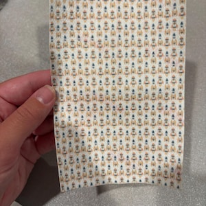 May include: A rectangular piece of paper with a repeating pattern of small rockets in orange, blue, and white. The rockets are evenly spaced across the surface of the paper. The paper is held by a hand.