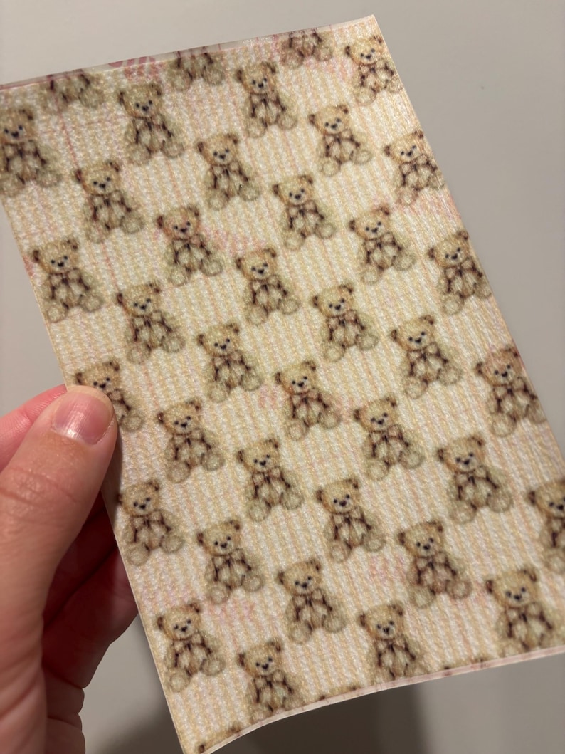 May include: A sheet of paper with a repeating pattern of small teddy bears. The bears are light brown with darker brown accents and bows. The background has a light pink and white striped design.