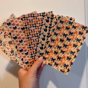 May include: A set of five rectangular sheets of faux leather fabric featuring various Halloween-themed patterns, including orange pumpkins, black bows, black cats, and white ghosts on light-colored backgrounds, arranged in a fan shape.