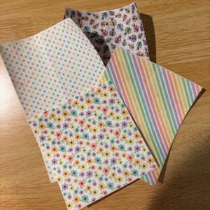 May include: Four sheets of patterned paper in pastel colors. One sheet has small polka dots, another has a floral pattern, a third has vertical stripes, and the fourth has a pattern of small flowers.