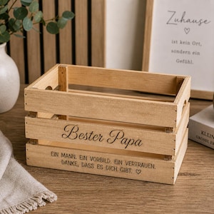 May include: A rectangular light brown wooden crate with open slats. The front panel features the engraved text Bester Papa, followed by the German phrase Ein Mann. Ein Vorbild. Ein Vertrauen. Danke, dass es dich gibt. with a small heart symbol.