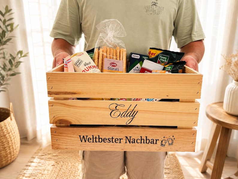 May include: A rectangular wooden crate filled with various food items, including a bag of breadsticks. The front of the crate features the name Eddy and the German text Weltbester Nachbar with two beer mug icons engraved on the bottom slat.