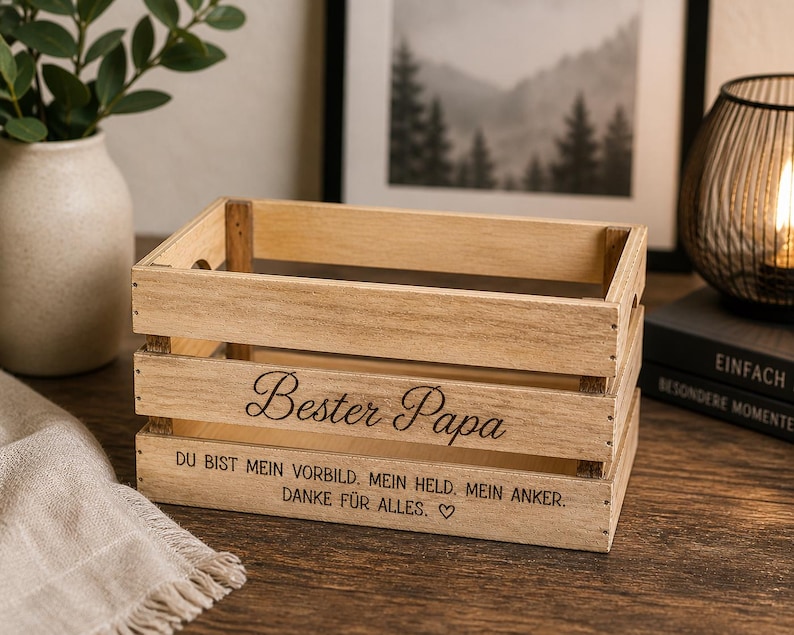 Könnte beinhalten: Eine rechteckige Holzkiste in hellem Braun mit offenen Lamellen. Auf der Vorderseite ist der Text "Bester Papa" in Schreibschrift eingraviert, gefolgt von "DU BIST MEIN VORBILD. MEIN HELD. MEIN ANKER. DANKE FÜR ALLES." und einem kleinen Herzsymbol.