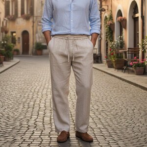 Man wearing beige linen trousers and light blue shirt walking down sunny cobblestone street.