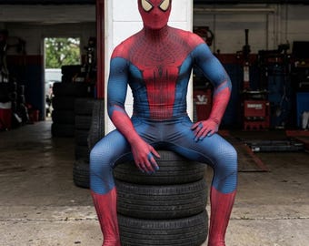 May include: A full-body spandex costume featuring a red and blue color scheme with a textured honeycomb pattern. The suit includes a mask with white eye lenses, a spider emblem on the chest, and red sections on the arms, legs, and torso.