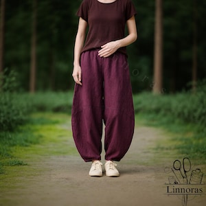 Könnte beinhalten: Eine Person trägt ein dunkelrotes T-Shirt und eine locker sitzende, dunkelviolette Hose. Die Hose hat eine einzigartige, abgerundete Form. Die Person trägt weiße Turnschuhe. Der Hintergrund ist eine verschwommene Waldszene.