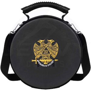 Puede incluir: Bolso redondo negro con asa y bandolera. El bolso presenta un emblema dorado con dos águilas, un triángulo y el texto "SPES MEA IN DEO EST". Tiene un asa negra y herrajes metálicos plateados.