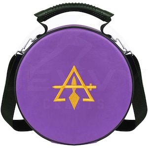 Op de afbeelding: Een ronde, paarse draagtas met een zwarte handgreep en schouderriem. De tas heeft een goudkleurig geborduurd embleem van een driehoek, speer en kruisontwerp. De tas heeft zilverkleurige metalen hardware.