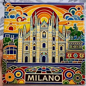 Könnte beinhalten: Ein farbenfrohes quadratisches Kachel mit einer stilisierten Illustration des Mailänder Doms, einer Straßenbahn und einer Statue. Das Design umfasst einen Regenbogen, Wolken und das Wort "MILANO" in einem braunen Banner. Die Kachel hat einen lebendigen, künstlerischen Stil.