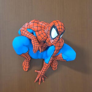 Op de afbeelding: Een Spider-Man-figuur in een gehurkte houding, voorzien van het iconische rood-blauwe pak met een zwart webpatroon. Het personage heeft grote witte ogen, een zwart spinnenembleem op de borst en staat in een dynamische, lage houding.
