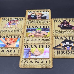 May include: A collection of seven rectangular One Piece wanted posters featuring Monkey D. Luffy, Roronoa Zoro, Nami, Sanji, and Brook. Each poster displays the character's name, a bounty amount, and the text WANTED DEAD OR ALIVE in black lettering.
