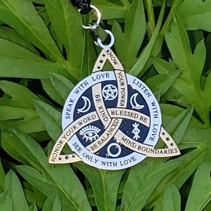 May include: A gold-colored pendant with a black cord necklace. The pendant is a triangle with a circle in the center and various symbols and phrases, including "Speak with Love" and "Mind Boundaries."