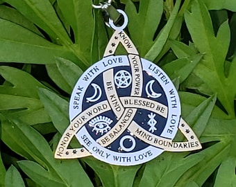 Puede incluir: Un colgante dorado con un collar de cordón negro. El colgante es un triángulo con un círculo en el centro y varios símbolos y frases, incluyendo "Speak with Love" y "Mind Boundaries".