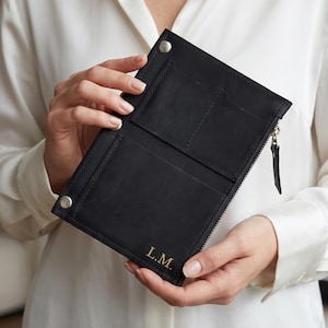 May include: A black leather wallet featuring a zippered side compartment, two snap button closures at the top corners, and the gold embossed initials L.M. on the bottom front corner. The wallet has multiple interior card slots visible.