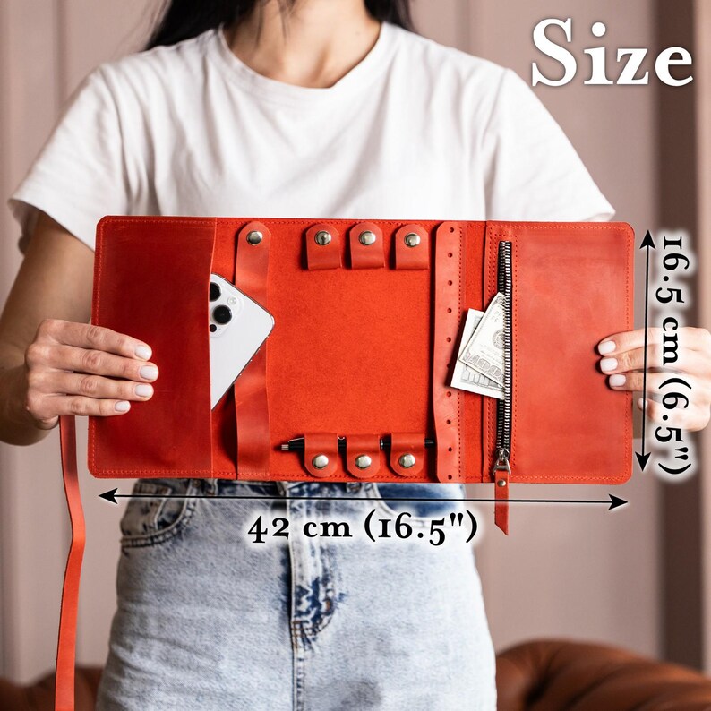 Może przedstawiać: Czerwony sk&oacute;rzany organizer podr&oacute;żny o szerokości 42 cm i wysokości 16,5 cm, z wieloma przegr&oacute;dkami. Posiada kieszeń zapinaną na zamek, zatrzaski i kieszeń na smartfon. Organizer przeznaczony jest do przechowywania biżuterii i innych drobnych przedmiot&oacute;w.