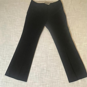 May include: Black flared pants. The pants have a high waist and a wide leg, creating a classic silhouette. The fabric appears to be a smooth, solid black material. The pants are laid flat on a light-colored surface.