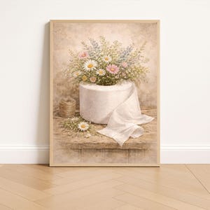 Puede incluir: Impresi&oacute;n enmarcada que muestra un rollo de papel higi&eacute;nico blanco desbordante de margaritas, flores silvestres rosas y azules. Una peque&ntilde;a bola de hilo y algunas flores sueltas est&aacute;n sobre una superficie de madera. Est&eacute;tica vintage.