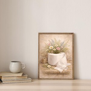 Puede incluir: Una impresi&oacute;n en acuarela enmarcada representa un rollo de papel higi&eacute;nico blanco rebosante de margaritas, flores rosas y azules. Una peque&ntilde;a bobina de hilo y flores sueltas est&aacute;n sobre una estanter&iacute;a de madera. La obra de arte tiene una est&eacute;tica vintage y r&uacute;stica.